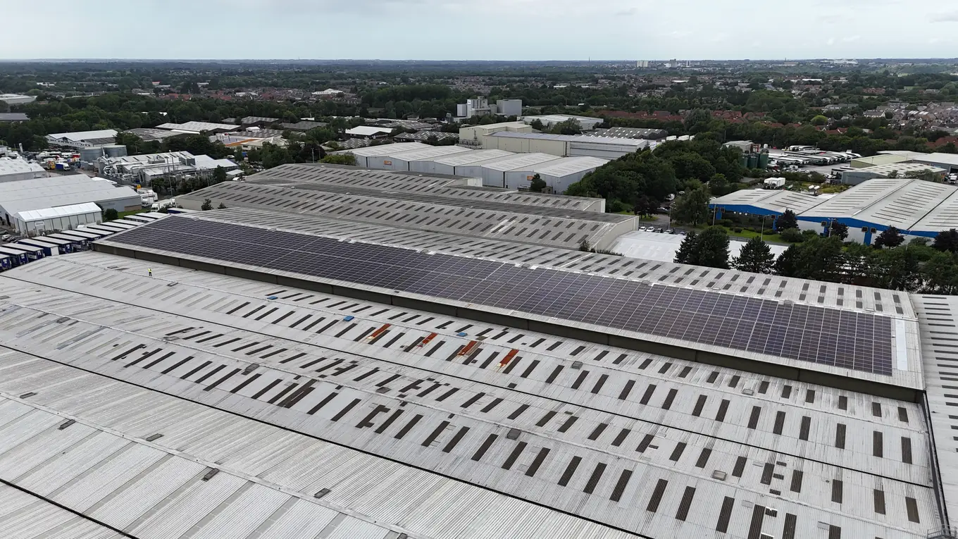 Solar array on a large industrial roof seen from above with the town skyline beyond