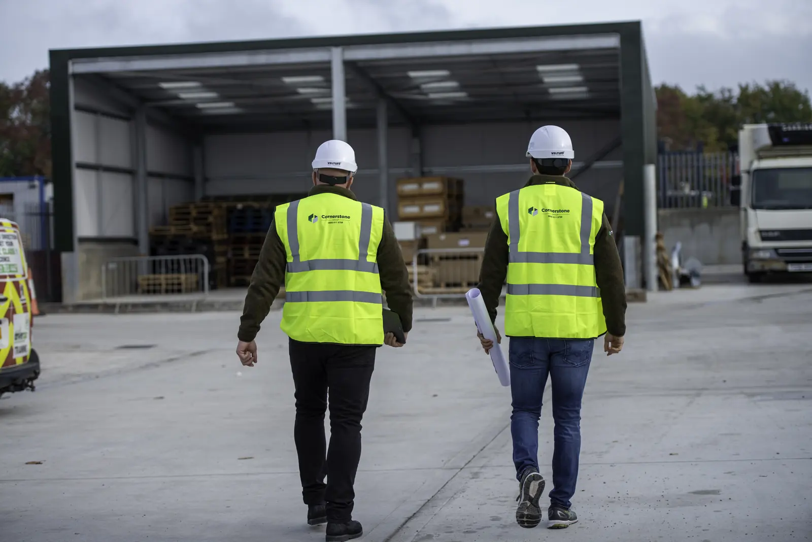 Two Cornerstone staff in hard hats and branded hi-vis walking towards a new steel framed canopy