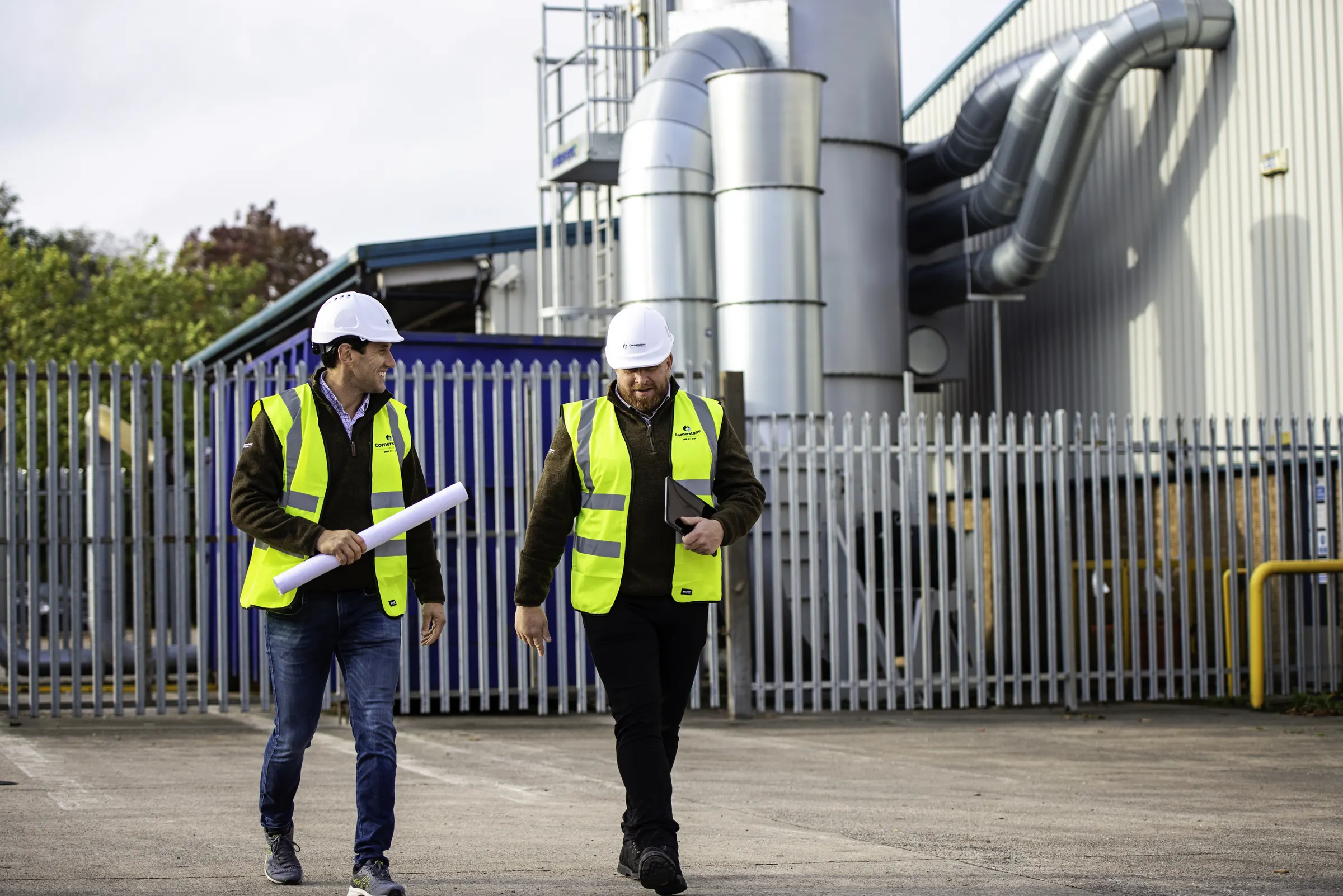 Two Cornerstone managers in hard hats and branded hi-vis walking across an industrial site
