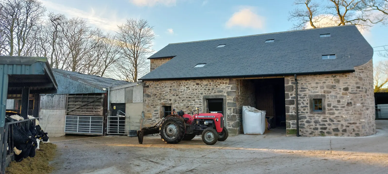 Restored stone barn at Fober Farm with a new slate roof and a red tractor in the farmyard