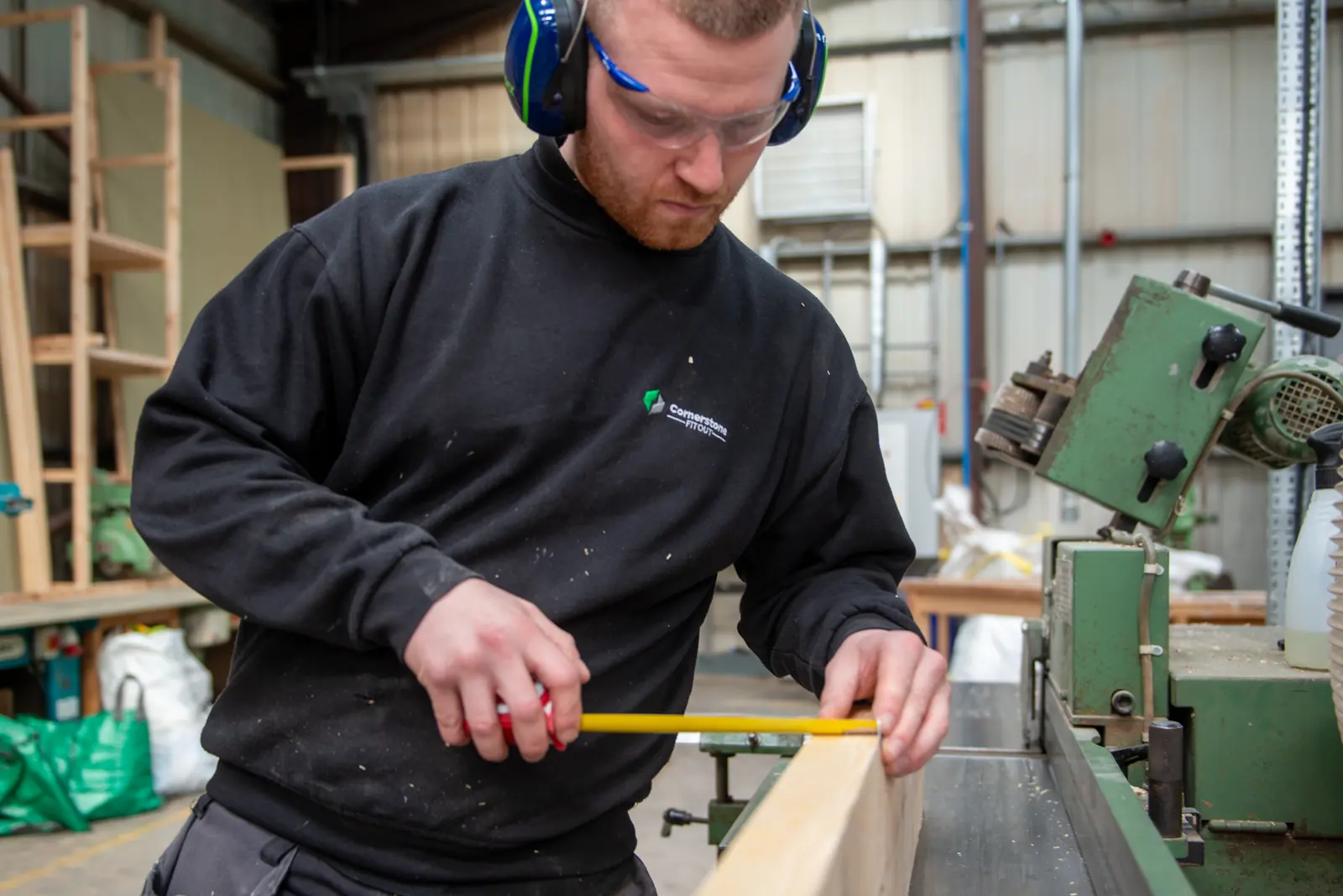 Cornerstone joiner in ear defenders and safety glasses measuring timber with a tape