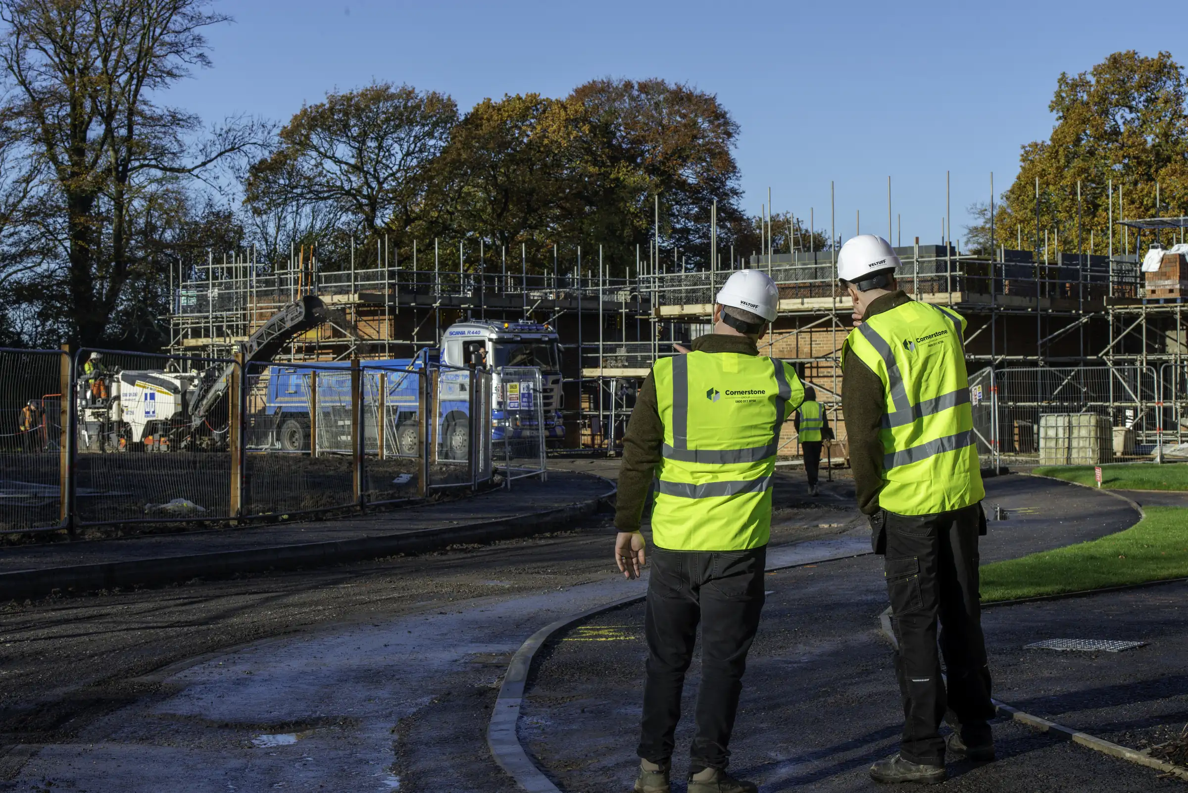 Two Cornerstone staff in hard hats and hi-vis overlooking a scaffolded housing development